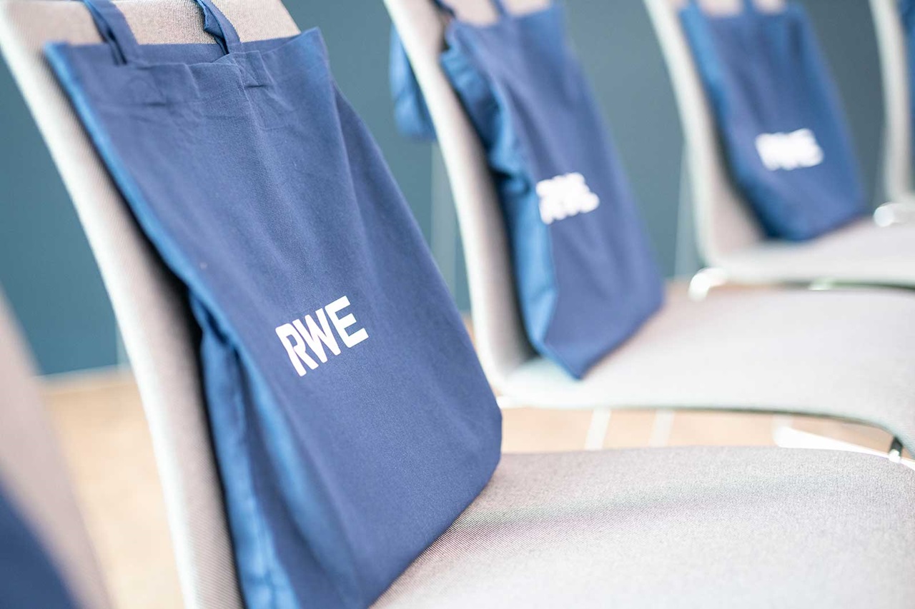 A row of chairs with blue bags labelled 'RWE' hanging on the back, set against a light blue wall.