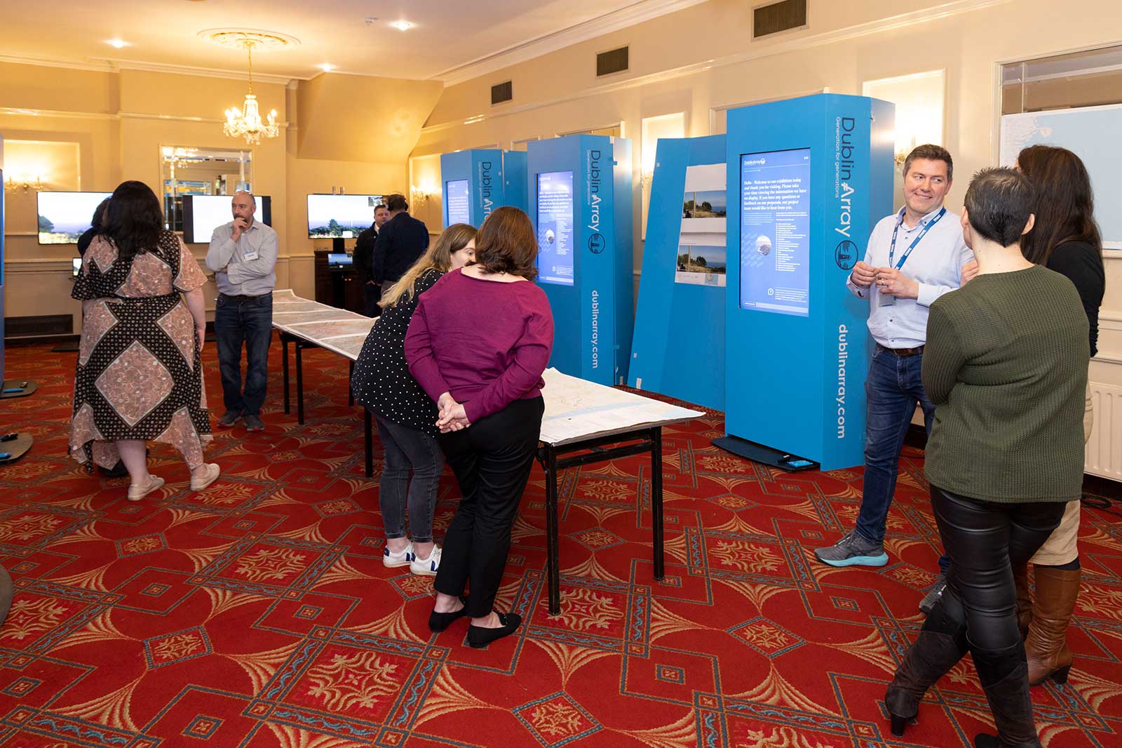 A group of people interacting with exhibition displays in a venue with a patterned carpet.