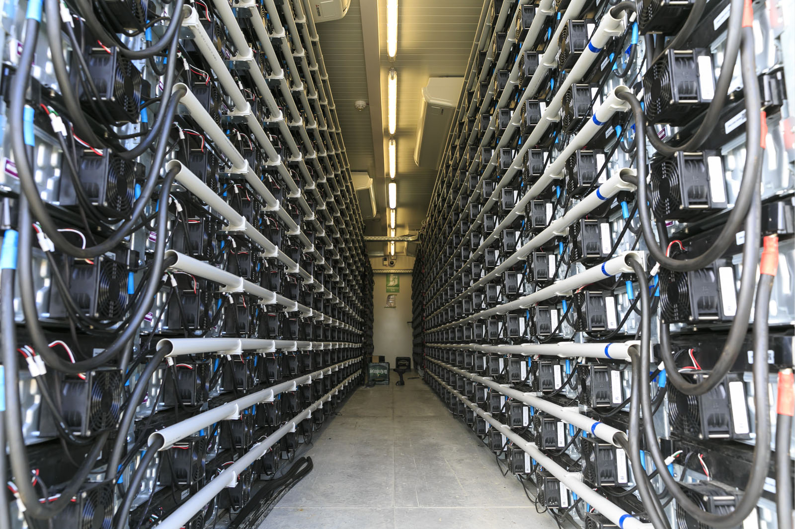 A narrow aisle between two rows of devices with cables in a modern technical room.